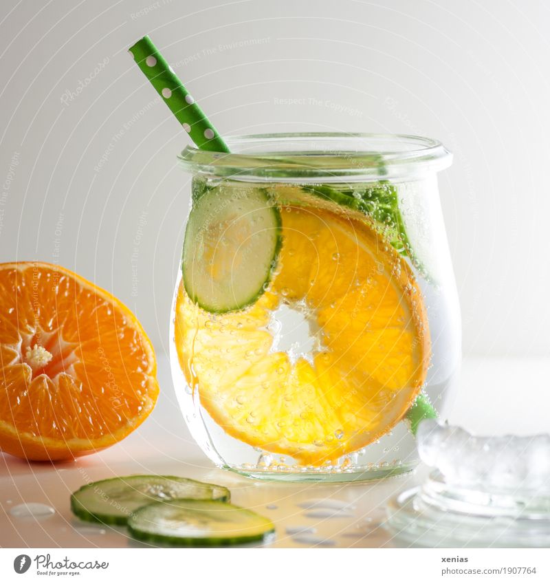 Cool soft drink with mineral water, tangerine, cucumber slices, ice cubes and green straw Cold drink Tangerine Slices of cucumber Ice cube Beverage Drinking
