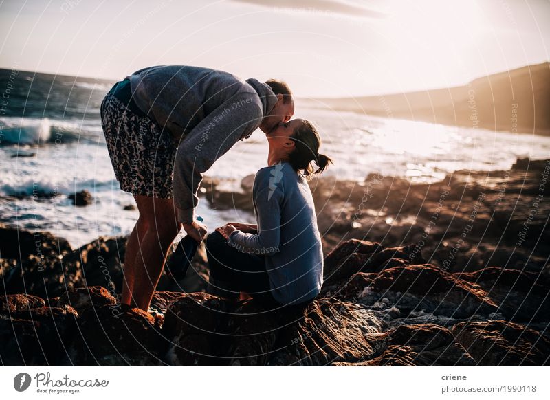 Happy young adult couple kissing at beach on rocks Lifestyle Joy Summer vacation Beach Ocean Young woman Youth (Young adults) Young man Couple Partner Rock