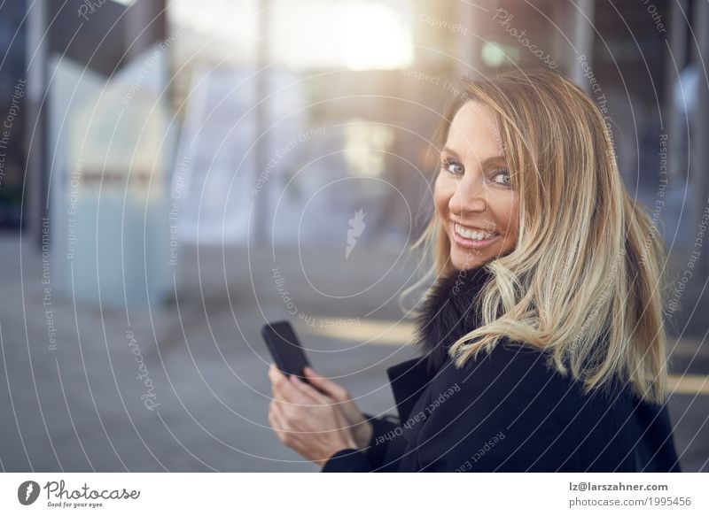 Smiling attractive woman looking over her shoulder Happy Face Business Telephone PDA Woman Adults 1 Human being 30 - 45 years Town Street Blonde Friendliness