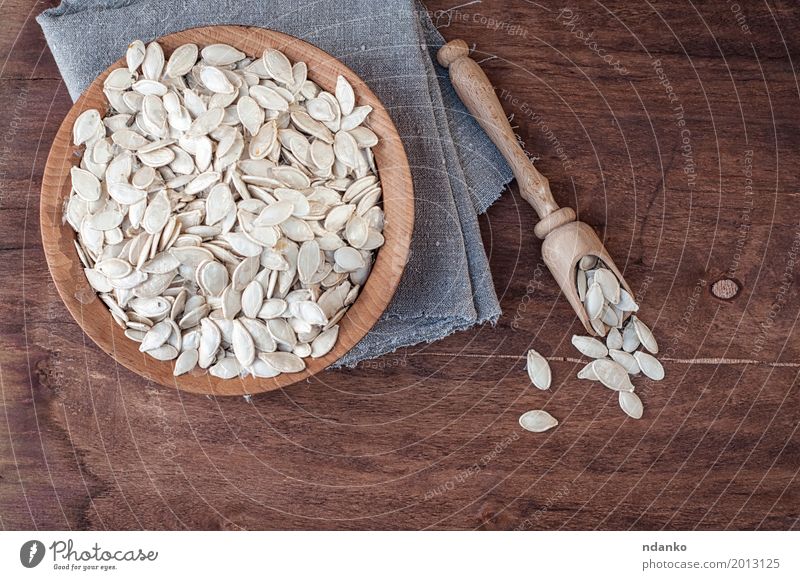 Unpeeled pumpkin seeds in a wooden bowl Vegetable Bowl Spoon Table Kitchen Wood Fresh Above Brown Gray White Snack Gourmet Top Tasty background board food Raw