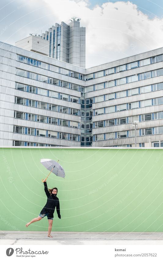 Woman with umbrella in front of a green wall, in the background skyscrapers Lifestyle Well-being Contentment Leisure and hobbies Playing Trip Adventure Freedom