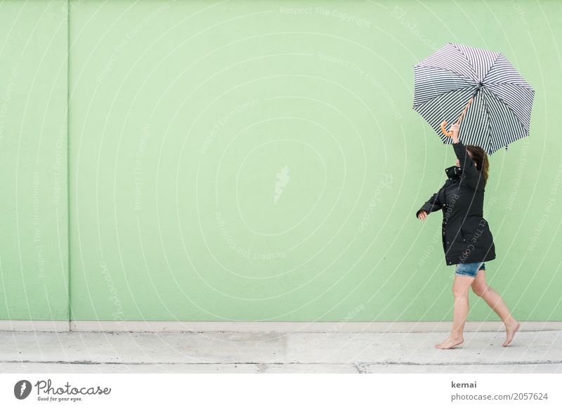 Woman walking with umbrella in front of green wall Lifestyle Style Harmonious Well-being Contentment Leisure and hobbies Playing Trip Freedom Human being