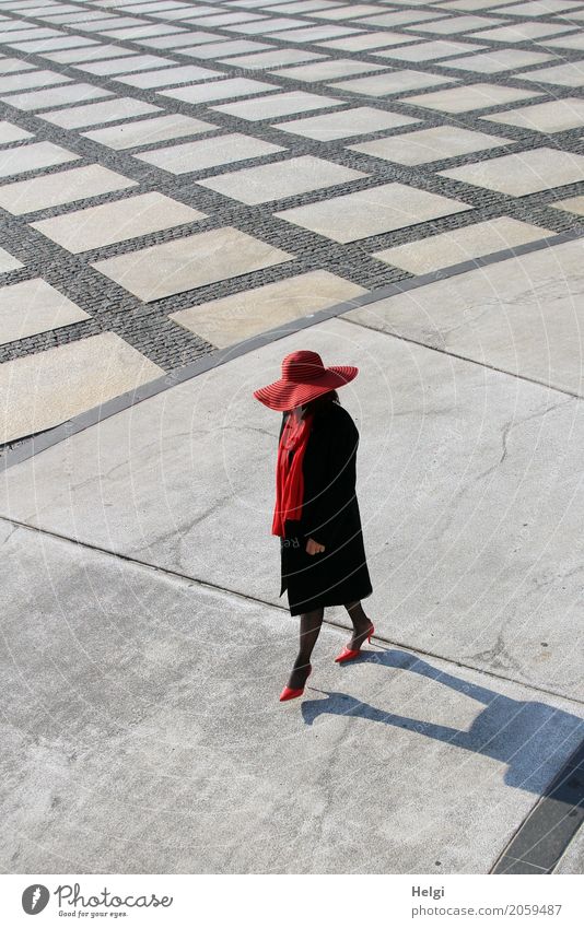 elegantly dressed lady with black coat, red hat, red scarf and red pumps walks on a large square with concrete and patterned floor Human being Feminine Woman