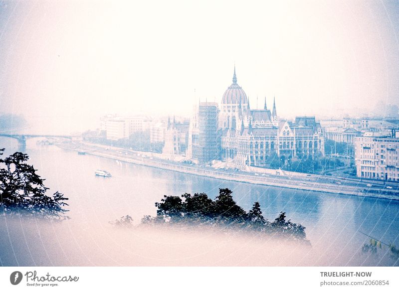 Budapest revisited, Parliament on the Danube, in the morning fog, from the high bank (Buda) opposite, a few ships, a Danube bridge and in the foreground the tops of trees