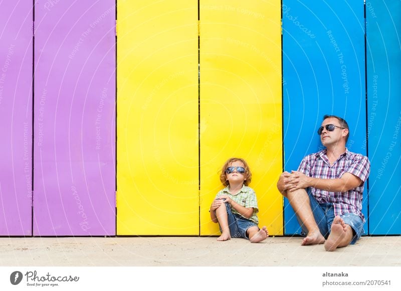 Father and son relaxing near the house at the day time. They sitting near are the colorful wall. Concept of friendly family. Lifestyle Joy Happy Relaxation