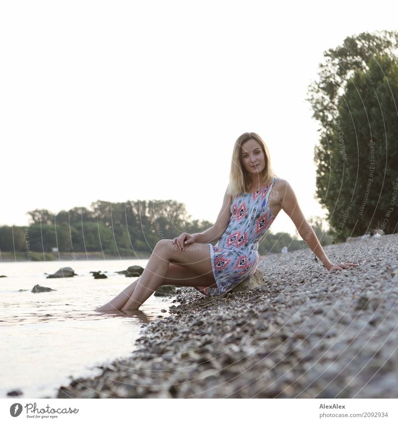 Young, slim woman in a summer dress sits on the banks of the Rhine with her feet in the water Joy pretty Life Well-being Young woman Youth (Young adults) Body