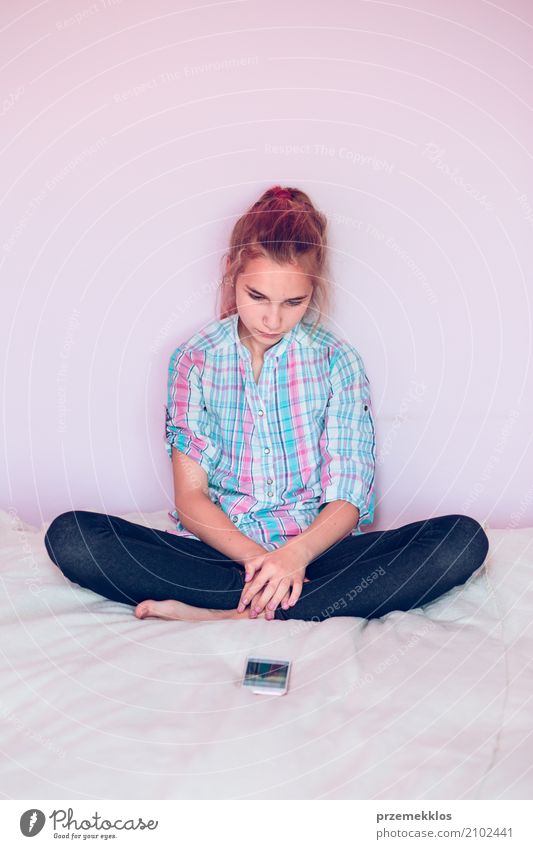 Young girl looking at mobile phone while sitting on bed Lifestyle Bedroom Child Telephone Cellphone PDA Technology Human being Girl Youth (Young adults) 1