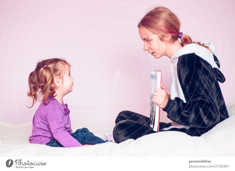 Girl showing the pictures in a book her younger sister Lifestyle Bed Child To talk Toddler Sister 2 Human being 1 - 3 years 13 - 18 years Youth (Young adults)