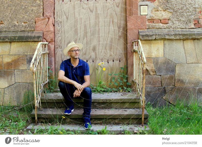 Man with beard, glasses and sun hat sits casually on a staircase in front of a dilapidated building Human being Masculine Adults Male senior Senior citizen 1