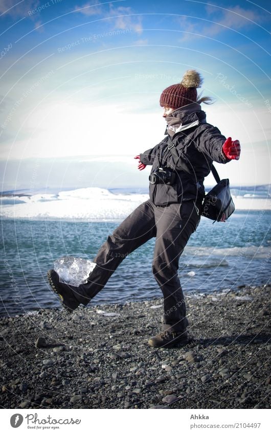 Young woman balances a chunk of ice on her foot while spreading her arms at the edge of a lake with ice floes Harmonious Meditation Adventure Far-off places