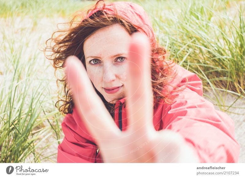 Young woman with windbreaker sits in the dune on the beach and shows the peace sign Lifestyle Vacation & Travel Tourism Trip Far-off places Freedom Summer