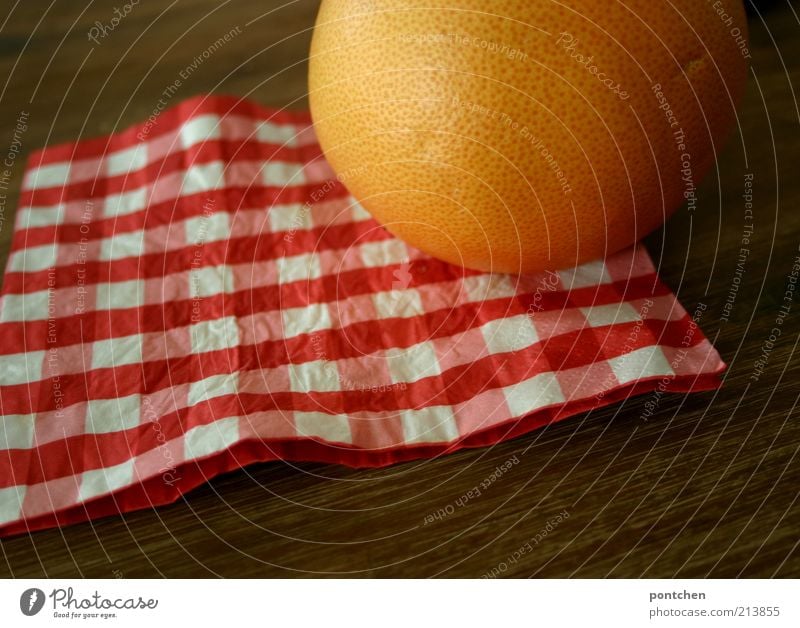 A grapefruit on a red and white checked napkin on a wooden table. Colours and companies. Round and square Food Grapefruit Nutrition Living or residing