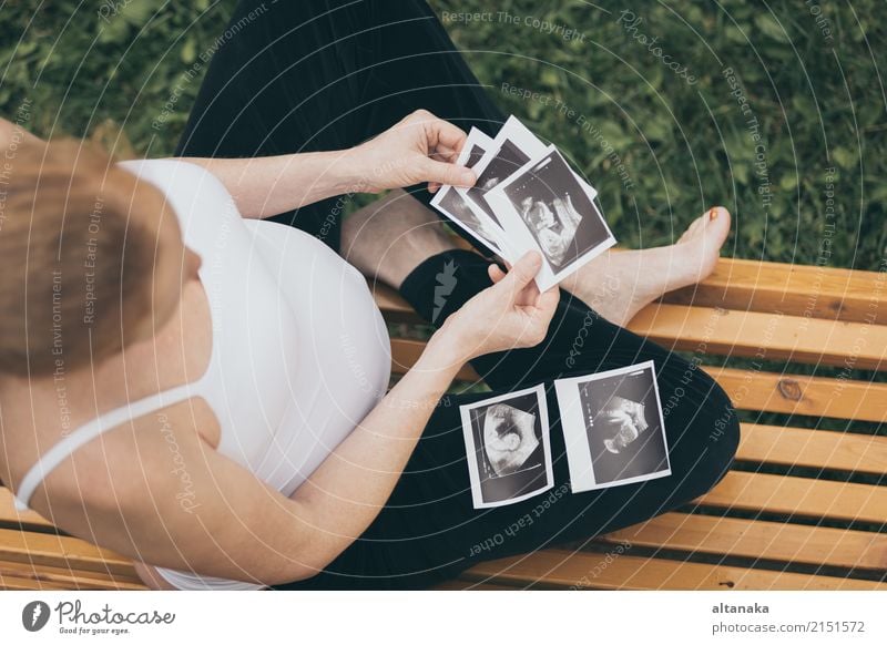 Pregnant caucasian woman resting at home. A young expectant mother reads a  doctor's report and looks at ultrasound pictures of her baby. Expectant mom  strokes her pregnant belly and thinks about baby 