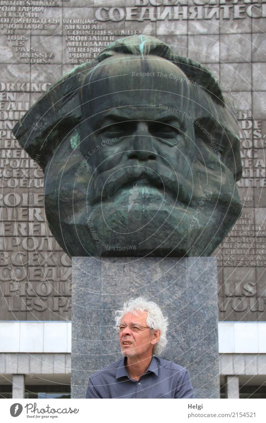 male senior with silver-grey curls, glasses and three-day beard sitting in front of the Karl Marx monument in Chemitz Human being Masculine Male senior Man
