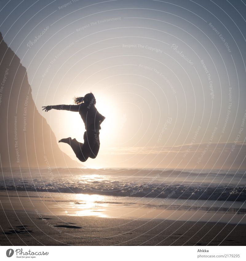 Young man jumping right in front of sun on beach by mountains in back light Athletic Fitness Life Contentment Senses Vacation & Travel Adventure Freedom