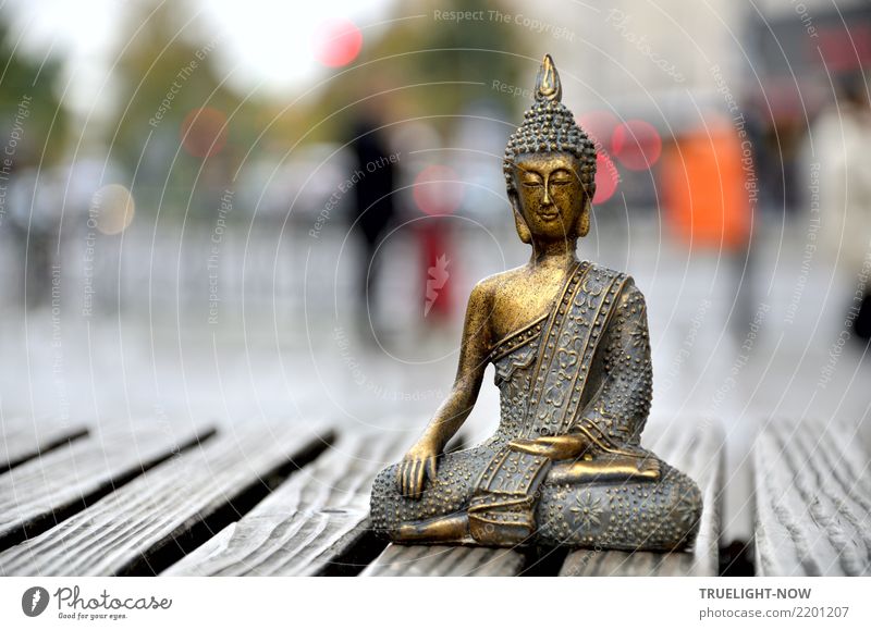 Small Buddha figure sitting in meditation posture on a bench in the middle of big city Harmonious Relaxation Calm Meditation Art Work of art Sculpture Downtown