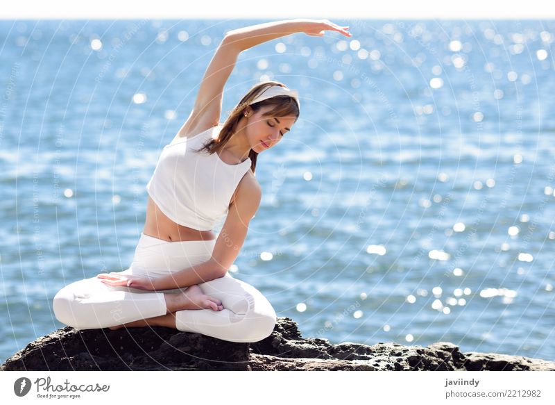 Meditation By Sex Young Women In White Dress On A Bridge By The Sea. Pretty  Woman Doing Yoga On The Beach. Sporty Woman Sitting In Yoga Position At Sea  View Background. Stock