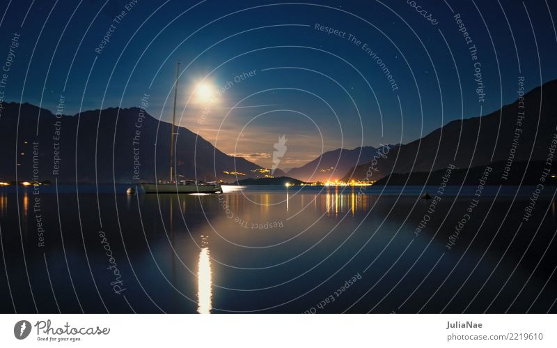 View of Lake Como at night Calm Mountain Water Moon Sailboat Watercraft Dark Moonlight Lago di Como Italy Lombardy Italian Mediterranean Lighting rays