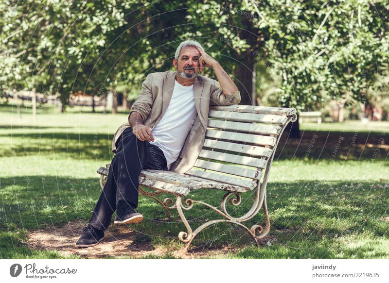 Pensive mature man sitting on a bench in an urban park. Lifestyle Happy Retirement Human being Man Adults Male senior 1 45 - 60 years Park Street Clothing Beard