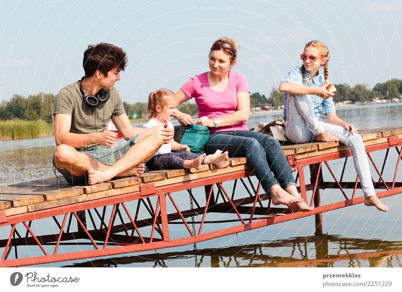Family spending vacation time together having a snack sitting on jetty over the lake on sunny day in the summertime Joy Happy Relaxation Leisure and hobbies