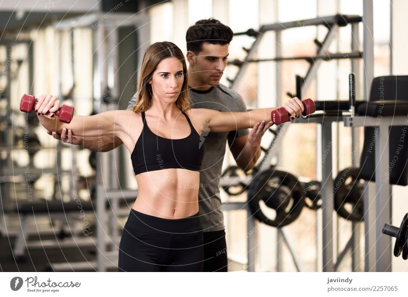 Personal trainer helping a young woman lift dumbells Lifestyle Body Sports Human being Masculine Feminine Young woman Youth (Young adults) Young man Woman