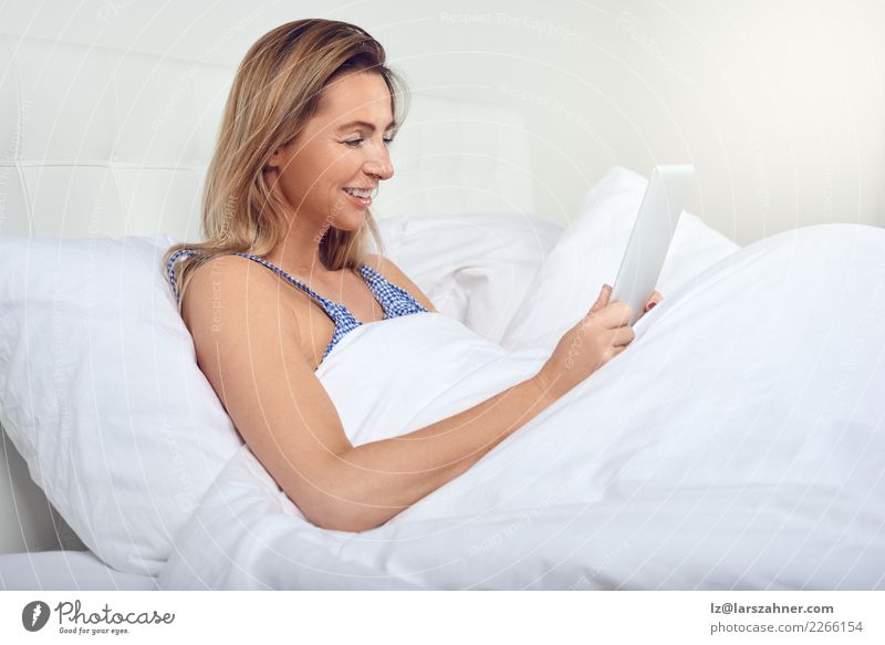 Attractive woman relaxing in bed with a tablet computer Shopping Joy Happy Beautiful Relaxation Bedroom Computer Technology Internet Woman Adults 1 Human being
