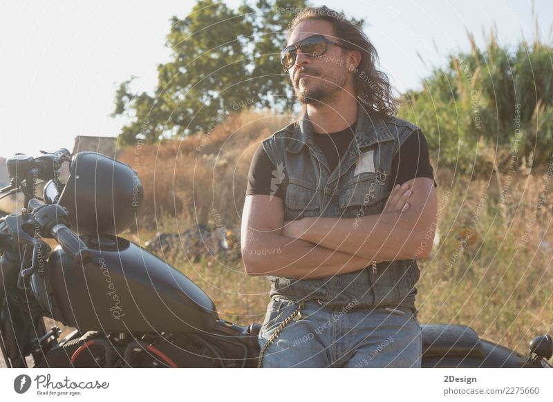 Long-haired brunette guy in sunglasses jeans and a jeans shirt posing on a black custom motorcycle Lifestyle Beautiful Vacation & Travel Trip Adventure Freedom