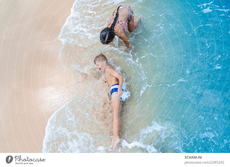Cute boy and girl having fun on the sunny tropical beach. Lying on sand, wonderful waves around them. View from above Lifestyle Joy Freedom Summer Island Child