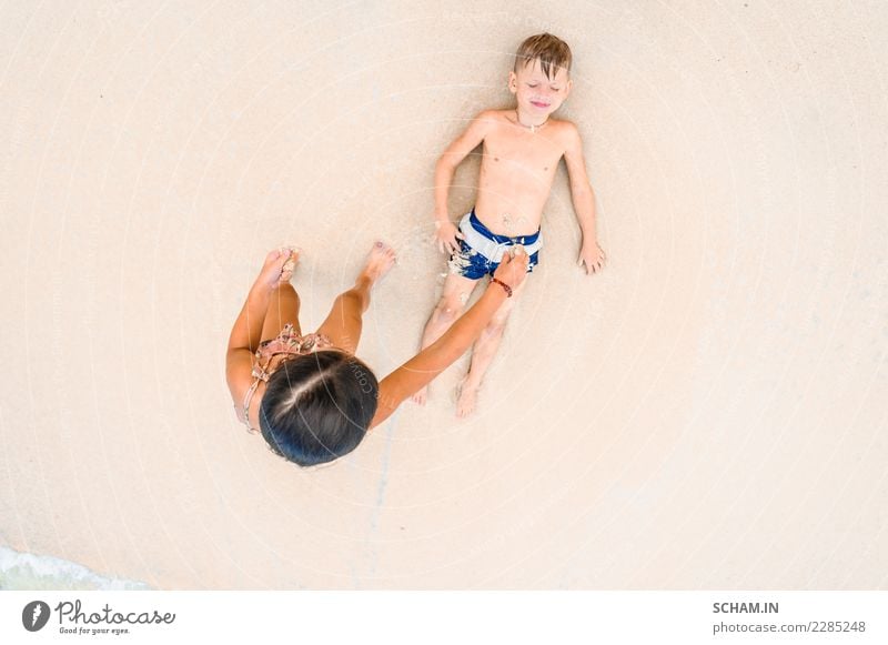 Cute boy and girl having fun on the sunny tropical beach. Lying on sand, wonderful waves around them. View from above Lifestyle Joy Freedom Summer Island Child