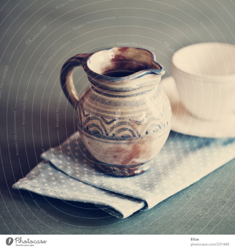 A painted ceramic milk jug next to an empty white cup Milk churn Pottery Cup already Napkin Vintage Blue Crockery Colour photo Interior shot Light