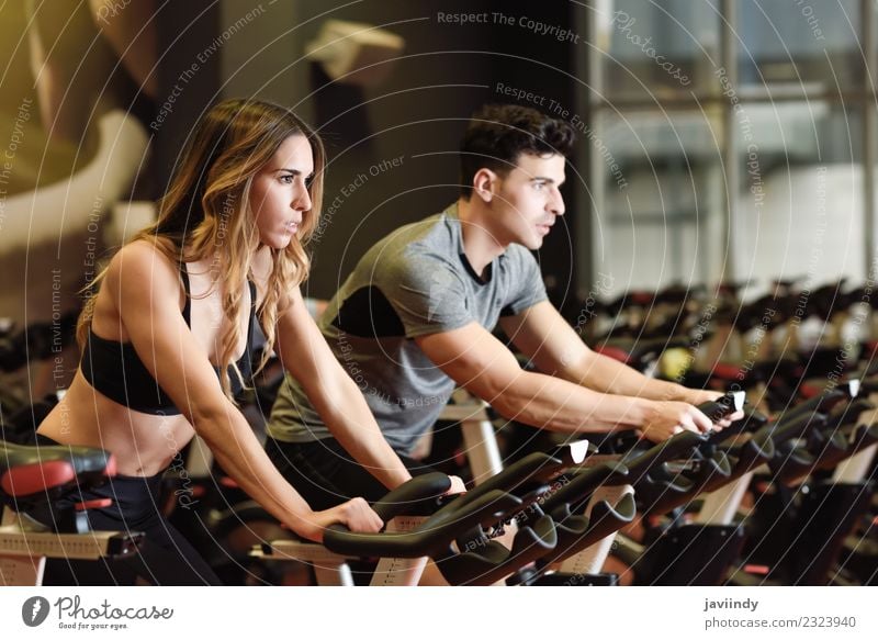 Two people biking in the gym, exercising legs doing cardio workout cycling bikes Lifestyle Leisure and hobbies Sports Work and employment Human being