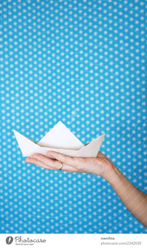 Hand holding a white paper boat against a blue background Design Leisure and hobbies Playing Children's game Origami Arts and crafts  Paper Paper boat