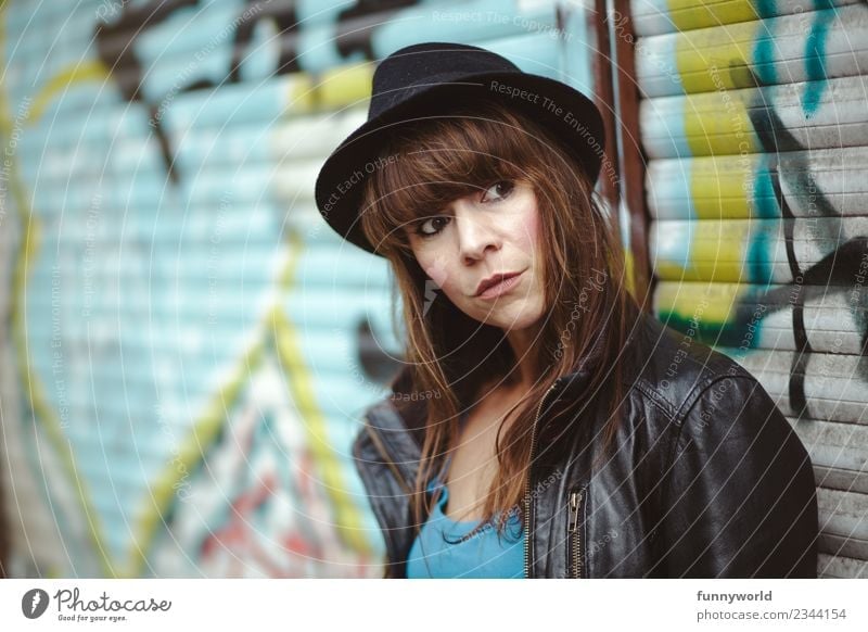 Woman stands before Graffiti and looks seriously to the side Human being Feminine Adults 1 30 - 45 years Cool (slang) Town Hat Bangs Brunette Skeptical Observe