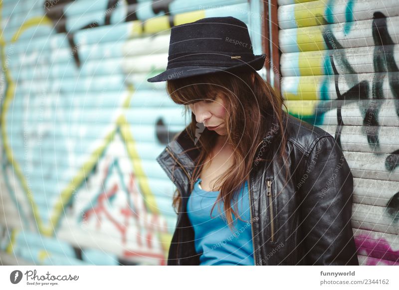 Woman standing in front of graffiti looking down. Feminine Adults 1 Human being 30 - 45 years Hat Cool (slang) Long-haired Leather jacket Graffiti Town Sadness