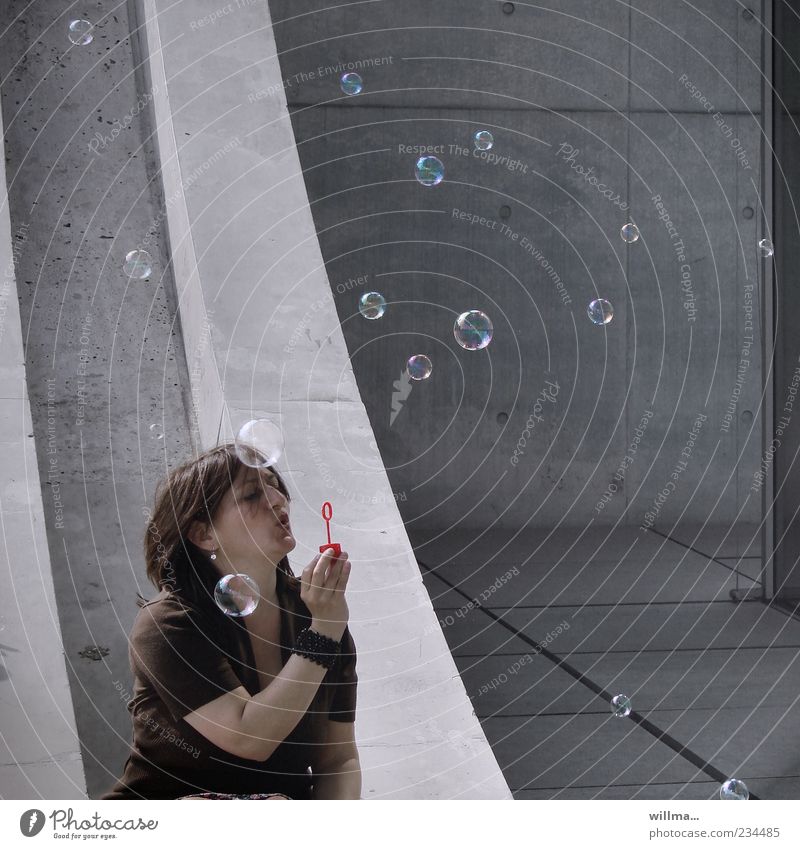 Woman sits in front of a concrete facade and blows her ears Soap bubble Adults 1 Human being 30 - 45 years 45 - 60 years Wall (barrier) Wall (building) Concrete