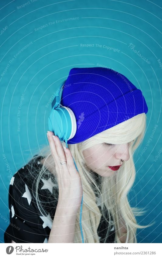 Young blond woman listening to music against a blue background Lifestyle Style Design Hair and hairstyles Leisure and hobbies Headset Technology