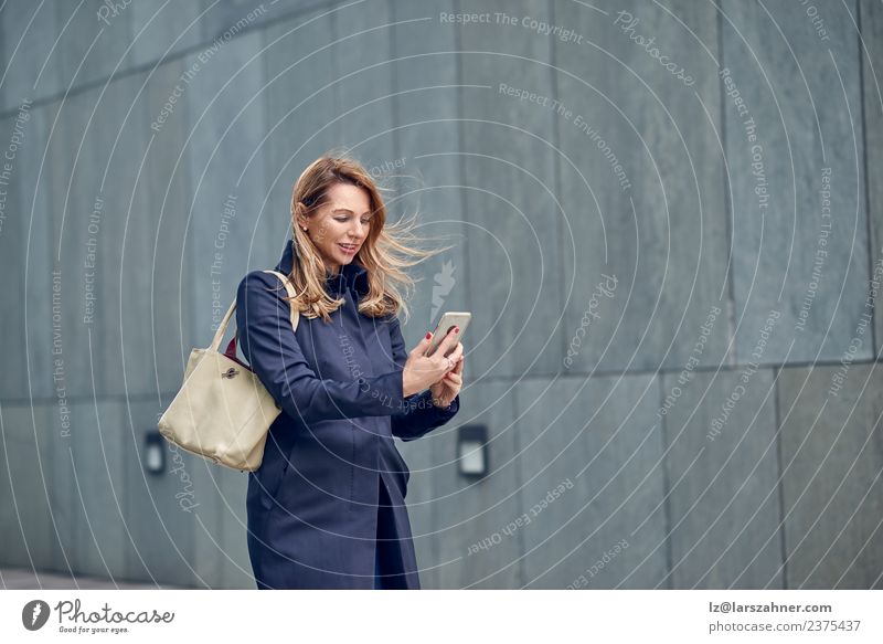 Middle-aged blond woman walking in the wind Face Reading Telephone Woman Adults 1 Human being 45 - 60 years Spring Wind Coat Blonde Concrete Movement Modern