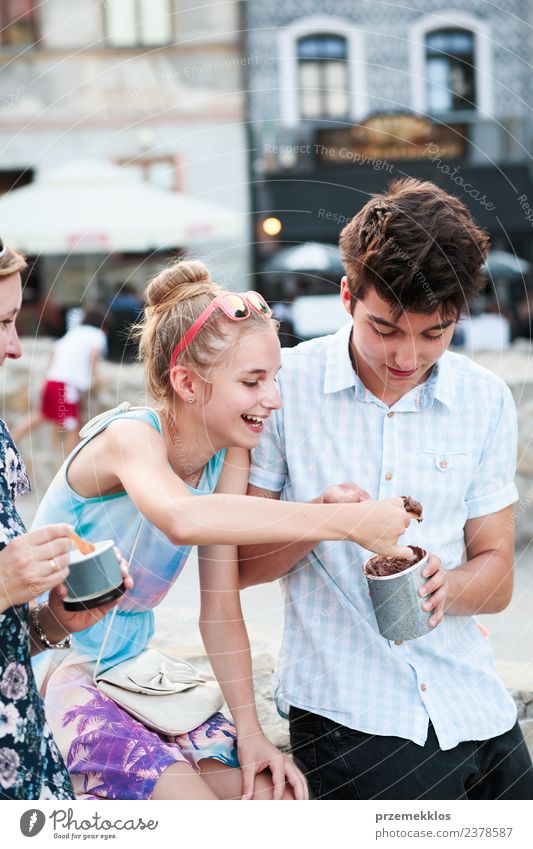 Family spending time together in the city centre enjoy eating ice cream on a summer day. Mother, teenage girl and boy spending quality time on sunny afternoon eating sweet dessert. Downtown area, old town in the background