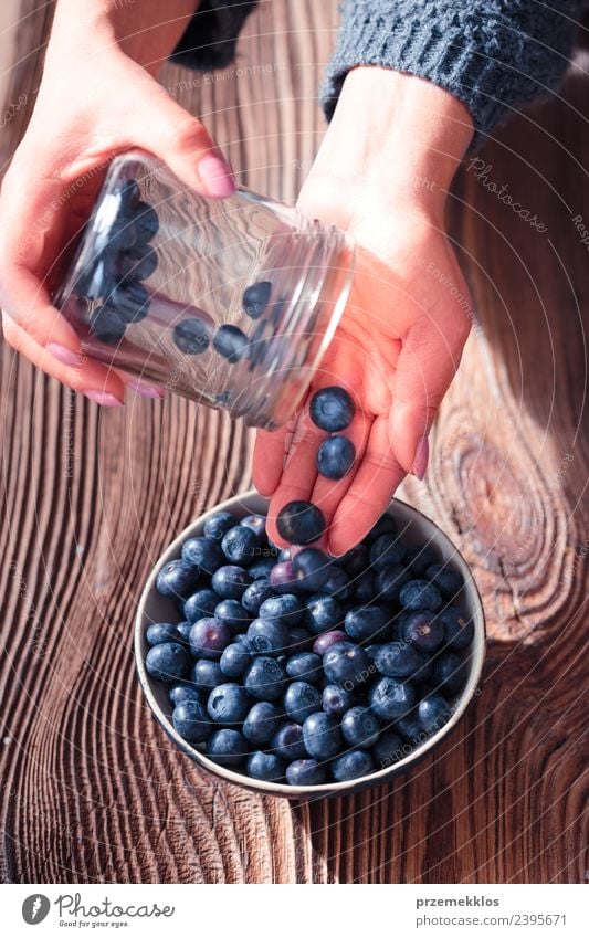 Woman putting fresh blueberries from a jar into a small bowl Food Fruit Nutrition Organic produce Vegetarian diet Diet Bowl Summer Table Adults Hand Nature Wood
