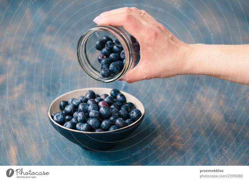 Woman putting fresh blueberries from a jar into a small bowl Food Fruit Nutrition Organic produce Vegetarian diet Diet Bowl Summer Table Adults Hand Nature