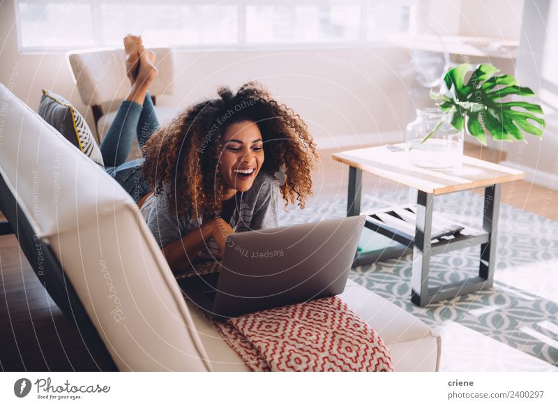 happy african woman lying on couch while using her laptop Lifestyle Happy Beautiful House (Residential Structure) Decoration Sofa Work and employment Computer