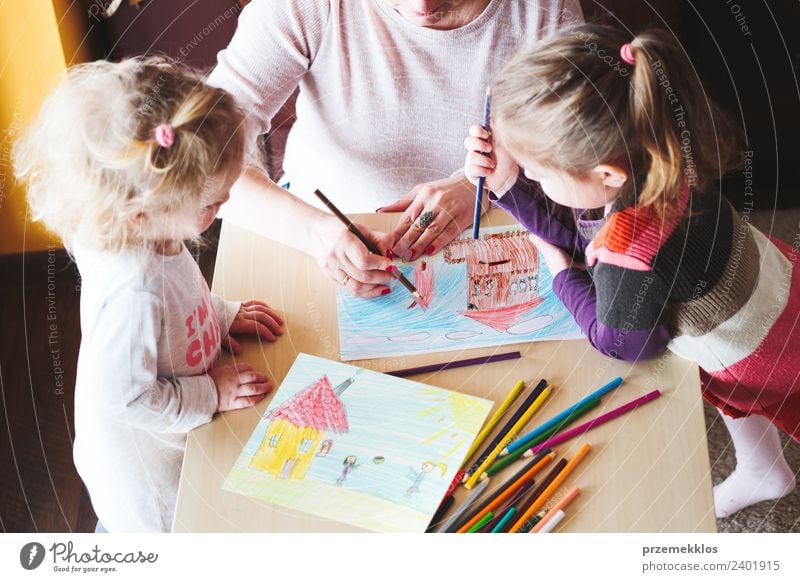 Mom with little girls drawing a colourful pictures of house and playing children using pencil crayons standing at table indoors Lifestyle Joy Happy Handcrafts