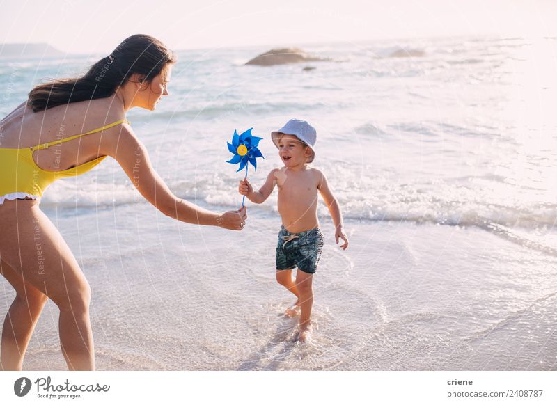 caucasian mother and son playing with windmill at the beach Lifestyle Joy Leisure and hobbies Playing Summer Sun Beach Ocean Child Woman Adults Mother