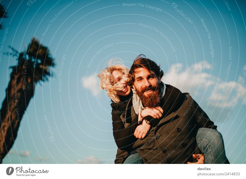 Bearded happy man carrying to her girlfriend in a piggyback way with blue sky in the background. Lifestyle Joy Leisure and hobbies Playing Human being