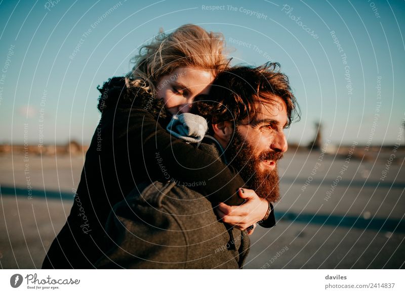 Bearded man carrying her girlfriend in a piggyback way outdoors at sunset. Lifestyle Joy Leisure and hobbies Human being Young woman Youth (Young adults)