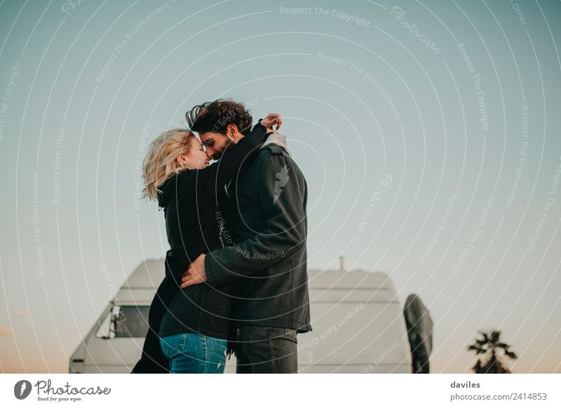 Blonde woman and bearded man embracing and smiling together with a van in the background at sunset. Lifestyle Joy Trip Camping Human being Young woman