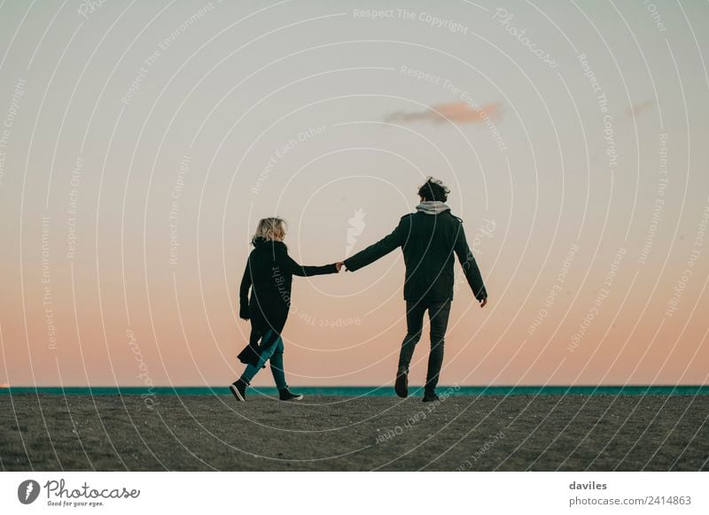 Young couple walking by the hand on the beach sand at dusk Lifestyle Joy Beautiful Vacation & Travel Beach Ocean Winter Human being Woman Adults Man Couple
