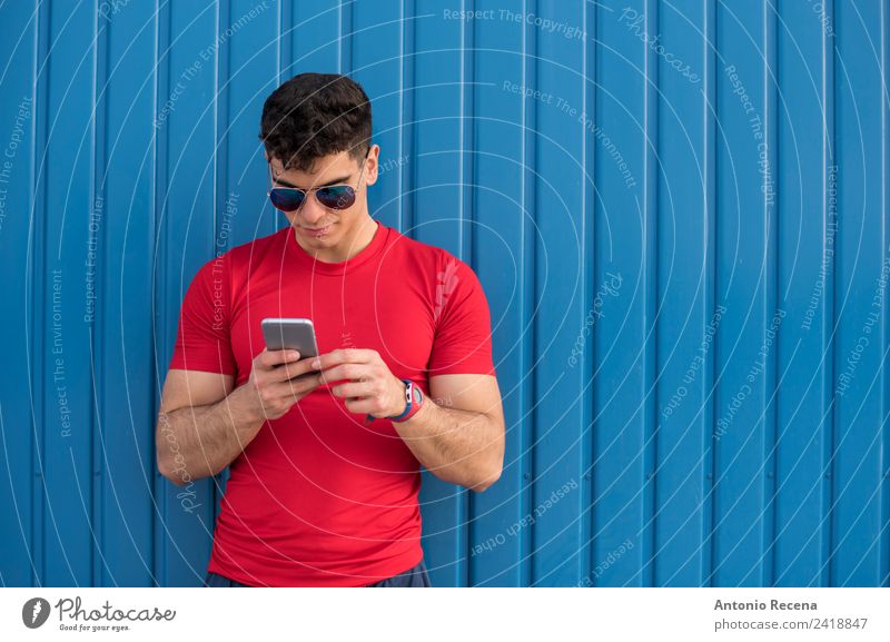 Red social on blue wall Reading Telephone PDA Human being Man Adults Sunglasses Brunette Touch Blue 20-25 years old 20s 30 years old attractive door Latin