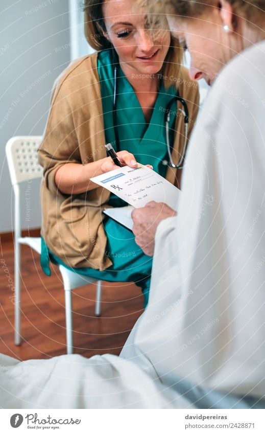 Doctor giving a prescription to senior patient Health care Medical treatment Illness Medication Chair Hospital Human being Woman Adults Pen Old Sit Authentic