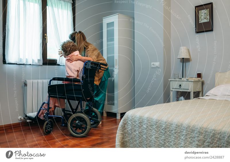 Caregiver with elderly patient in a wheelchair in front of window Lifestyle Health care Illness Medication Doctor Hospital Human being Woman Adults Slippers Old